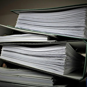  A large stack of organized paper documents is shown on a desk.
