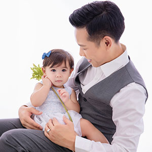 Attorney David Nguyen in formal attire holding his baby girl in a white dress. - Law Office of David Nguyen, PC.