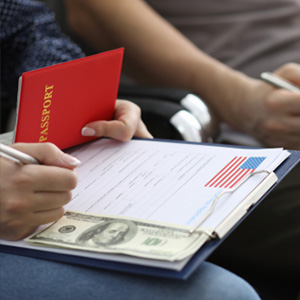 Filling out a spousal Green Card application with passport and cash; cost of U.S. immigration fees.
